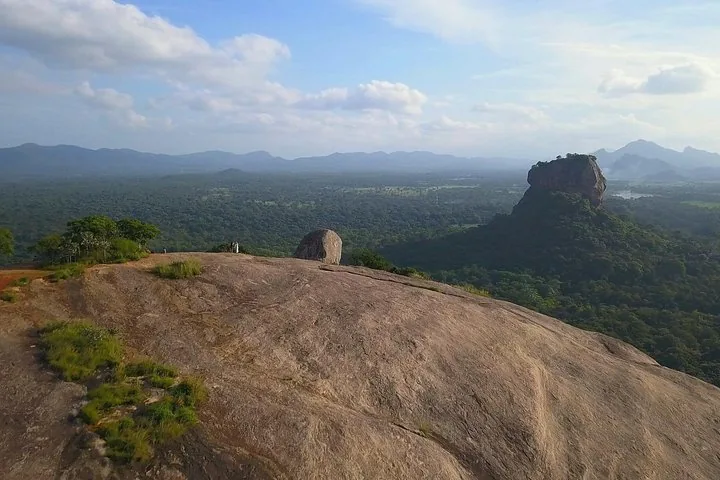 Personen stehen am Rand des Pidurangala-Felsens und betrachten Sigiriya