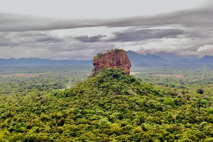 Der Sigiriya-Felsen ragt unter bewölktem Himmel über dichten grünen Wald empor